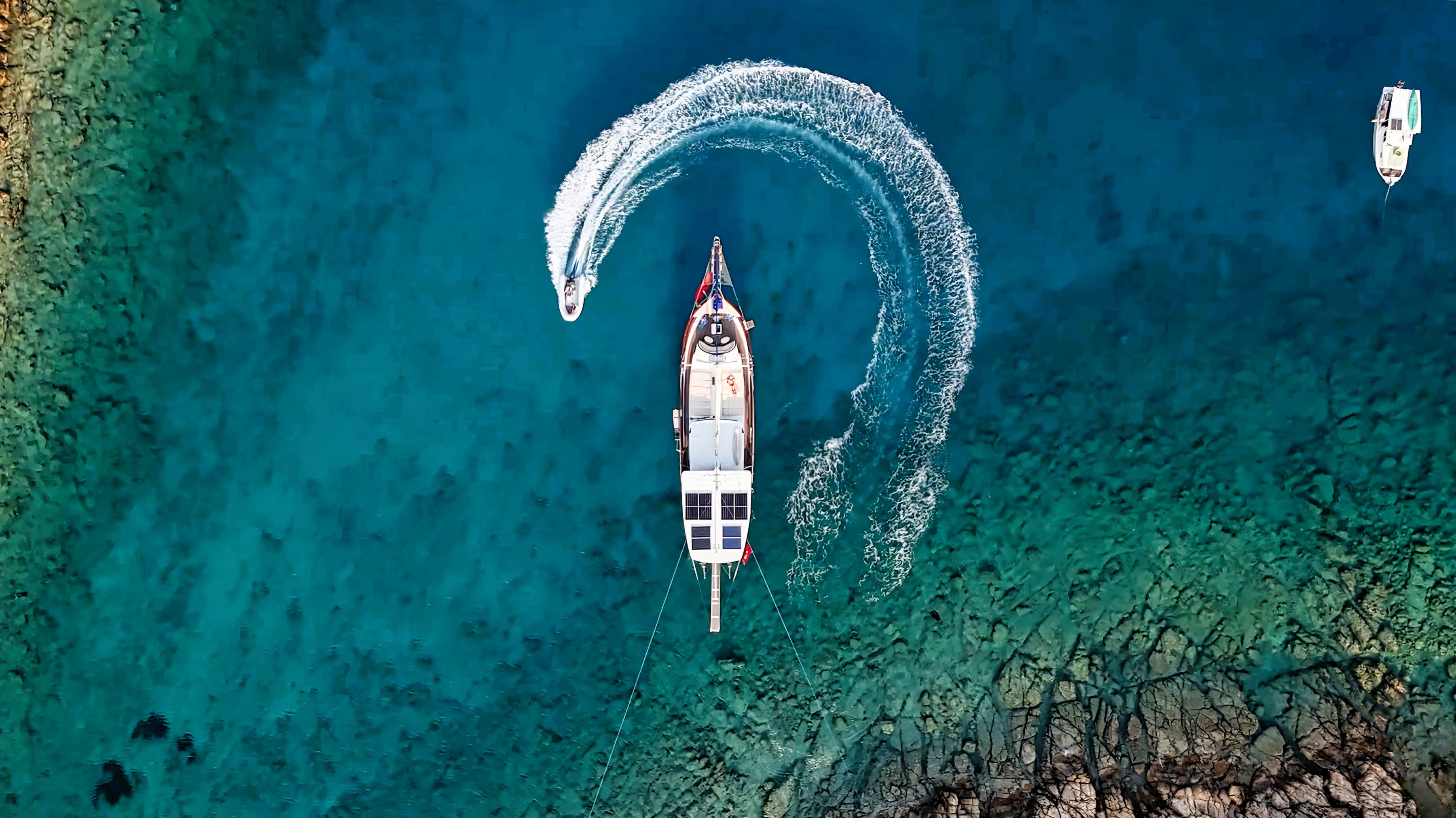 Seen from above: a gulet at anchor in clear turquoise water, her tender circling beside her