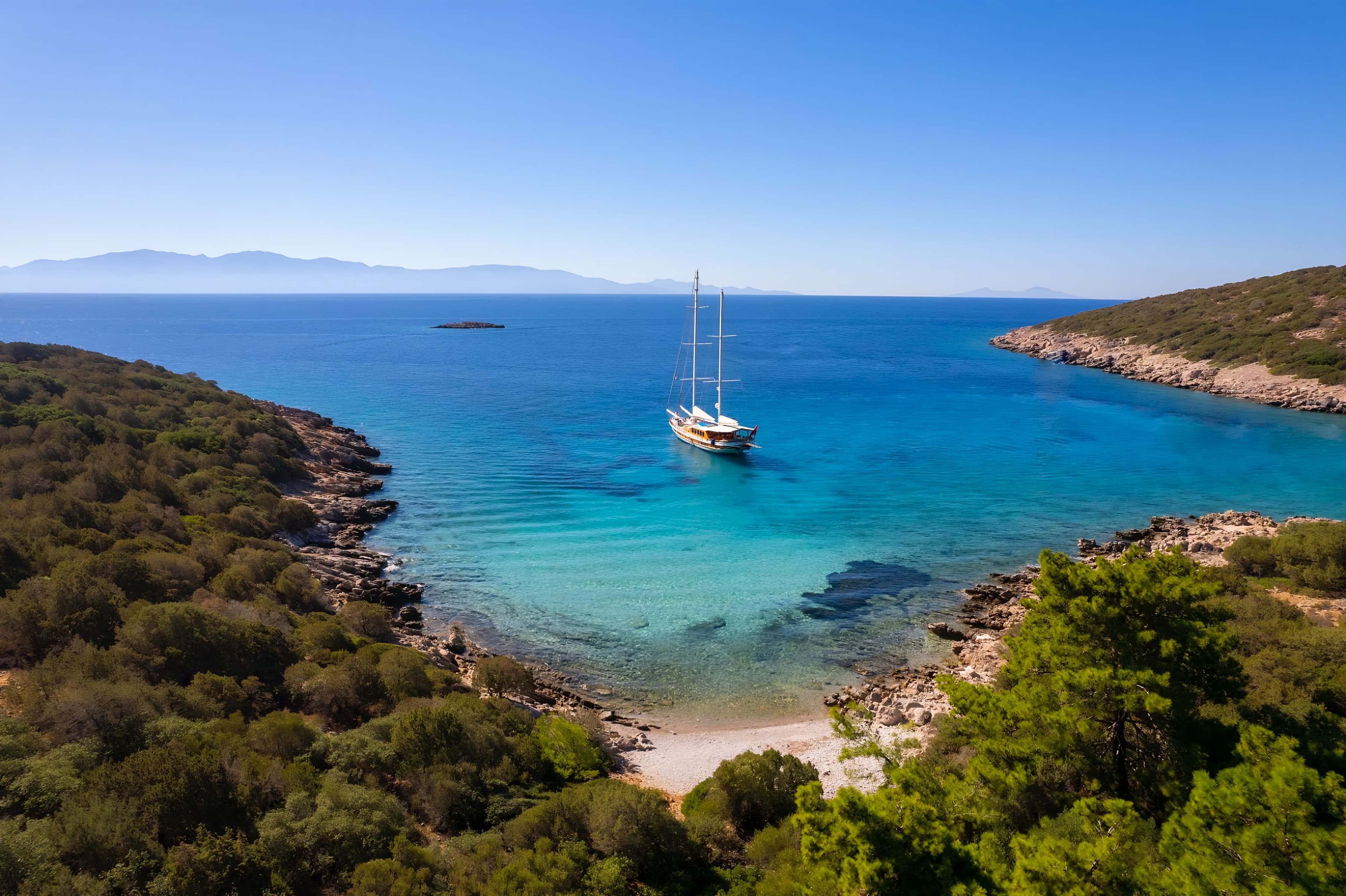 A two-masted gulet at anchor in a turquoise bay, with pine trees and a small beach in the foreground